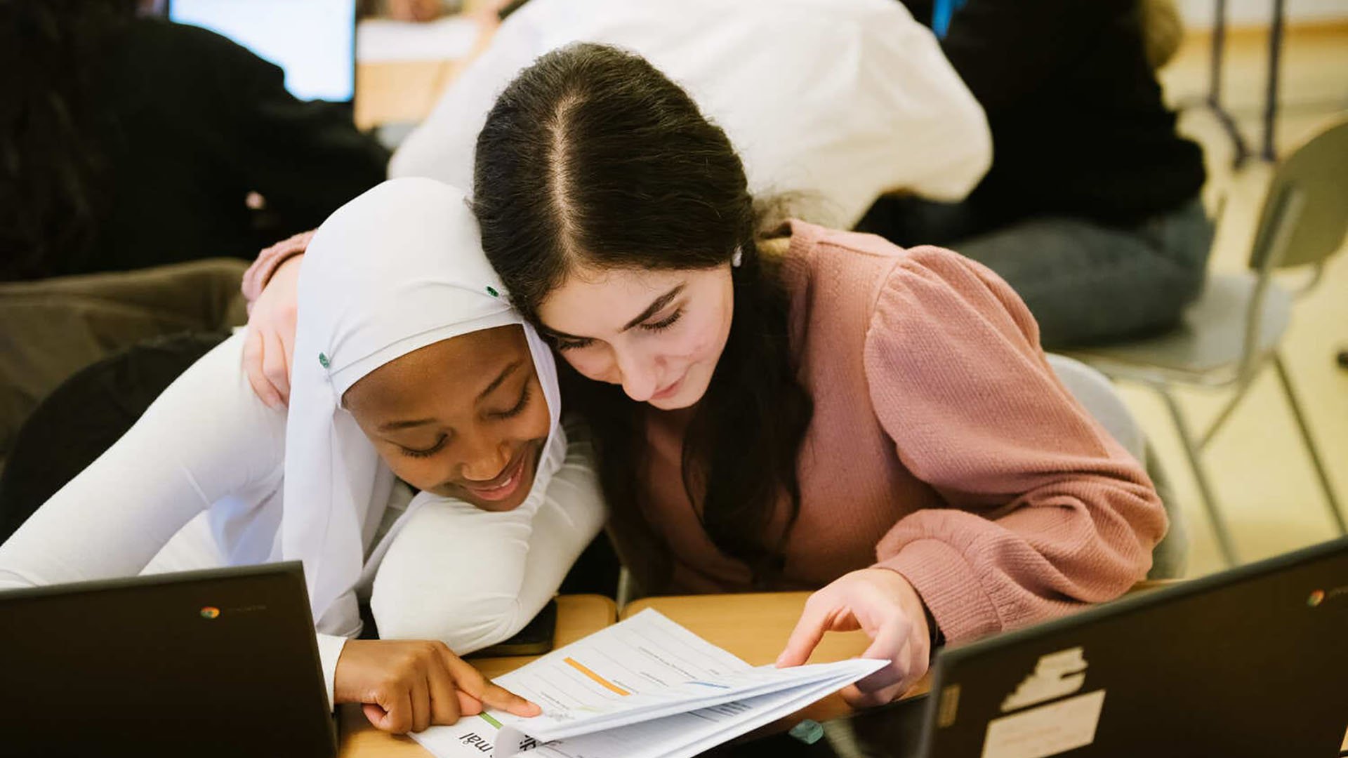 Två personer studerar tillsammans vid ett bord med datorer.
