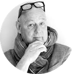 Porträtt av en man med glasögon på huvudet, iförd halsduk och blazer, med handen vid hakan